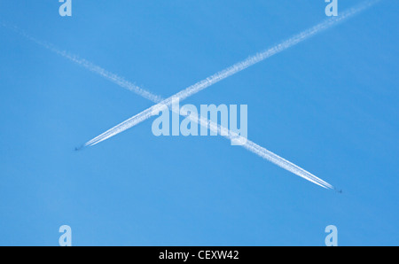 Aeromobile contrails crossing e formando una X in un cielo blu Foto Stock