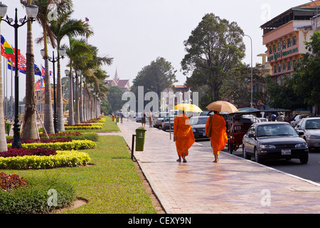 Due monaci in abiti dello zafferano proteggersi dal sole con ombrelloni mentre si cammina sulla strada a fianco di Sisowath Quay Foto Stock