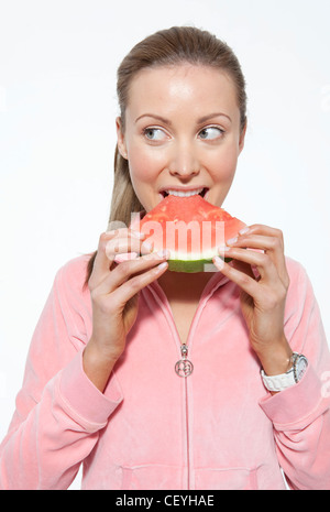 Femmina con capelli biondi legati a coda di cavallo, indossa una camicia rosa, mangiando anguria, sorridente, guardando al lato Foto Stock