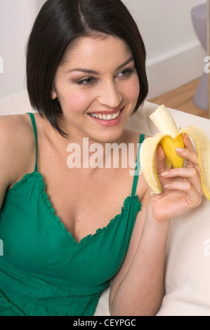 Femmina con lunghezza mento dritto brunette capelli mangiando una banana, sorridere mostrando i denti Foto Stock