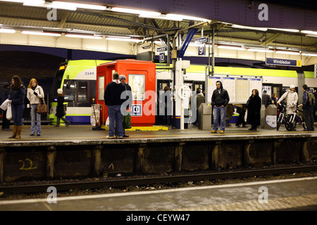 I passeggeri in attesa di un treno su una piattaforma a Wimbledon stazione ferroviaria di sera. Foto Stock