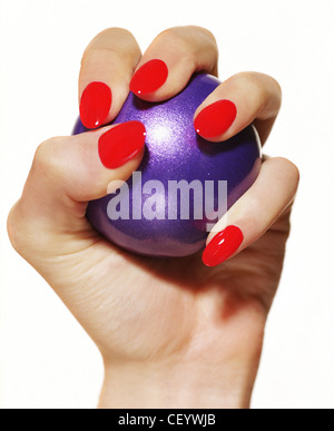 Indossare femmina rosso brillante smalto per unghie schiacciando un viola palla nel palmo della sua mano Foto Stock
