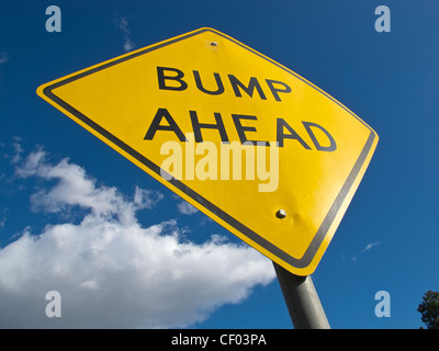 Giallo cartello stradale con la scritta nera di avvertimento del "bump ahead' come visto da un angolo basso contro il profondo blu del cielo. Foto Stock