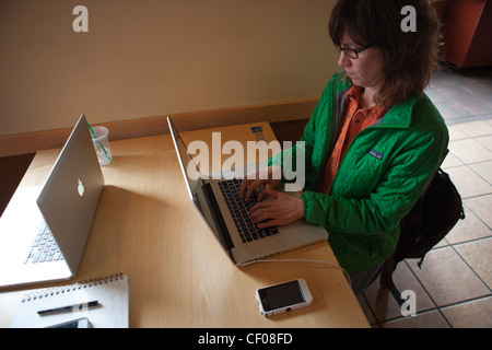 Donna digitando su Mack laptop in un coffee shop con iphone. Foto Stock