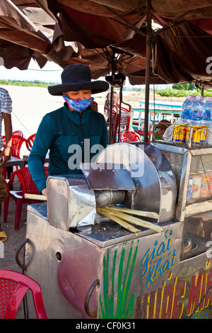 Donna premendo la canna da zucchero per fare il succo in Hoi An, Vietnam Foto Stock