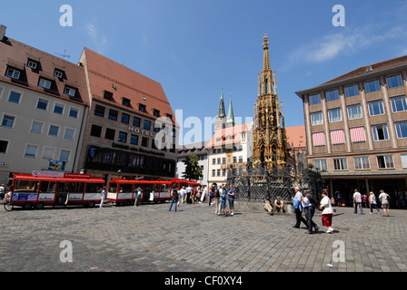 Un treno turistico rosso parcheggiato nella piazza principale del mercato di Norimberga (Hauptmarkt), in Baviera, Germania, accanto allo Schoner Brunnen, risalente al 14th° secolo. L'oro Foto Stock