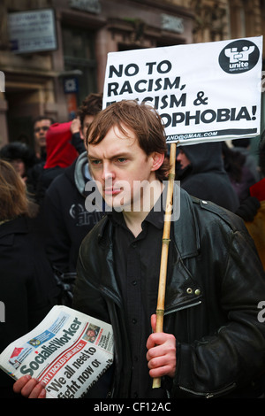 Giovane uomo che porta un anti-razzismo banner e vendita " il lavoratore socialista" durante una manifestazione in strada, Glasgow Foto Stock