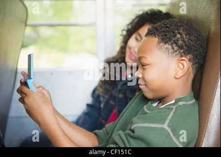 Ragazza ragazzo di guardare la riproduzione del video gioco su bus di scuola Foto Stock