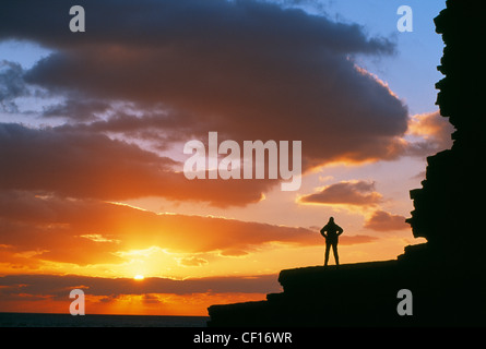 Una figura solitaria sorge arroccato sulla cima di una scogliera a Nash punto silhoutted al tramonto. Foto Stock