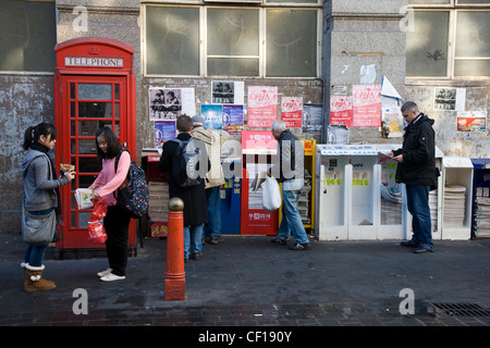 La gente di raccolta e libera lettura giornali cinesi da un edicola in Chinatown, Londra Foto Stock