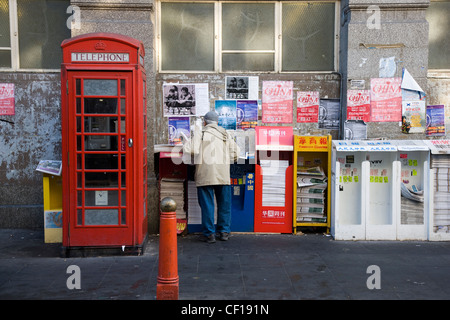 La gente di raccolta e libera lettura giornali cinesi da un edicola in Chinatown, Londra Foto Stock