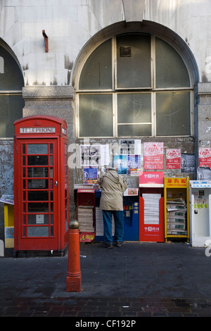 La gente di raccolta e libera lettura giornali cinesi da un edicola in Chinatown, Londra Foto Stock