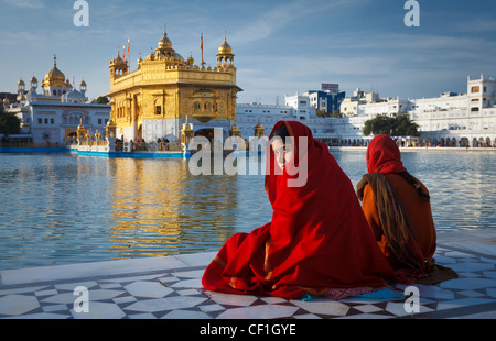 Due donne indiane vestito di rosso sari davanti al tempio d'oro di Amritsar Punjab, India Foto Stock