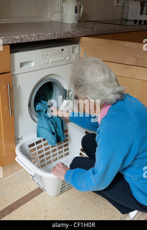 Signora il caricamento di una macchina di lavaggio in una camera di servizio o di utilità, Inghilterra, Regno Unito. Foto Stock