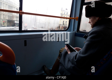 Una moda giovane donna che indossa un cappello di pelliccia la lettura di un Kindle libro elettronico seduto alla parte superiore del finestrino anteriore di un autobus a due piani a Londra REGNO UNITO Foto Stock