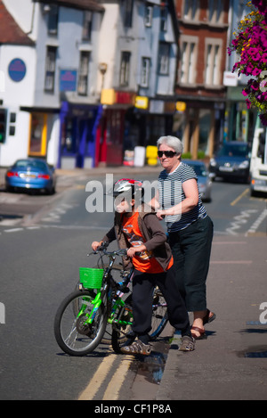 Nonna e nipote spingendo le loro biciclette attraverso una strada a Abingdon. Foto Stock