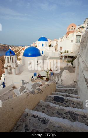 Una vista verso il basso un piccolo percorso di avvolgimento verso una serie di cupole blu greco chiese ortodosse nel villaggio di Santorini Foto Stock