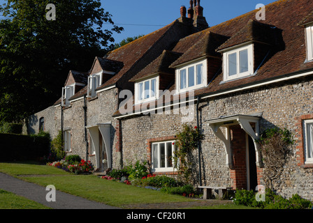 Una linea di tradizionali case di pietra focaia al confine con il villaggio verde nel villaggio di East Dean vicino a Beachy Head. Foto Stock