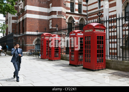 Un imprenditore a camminare lungo una fila di tradizionali cabine telefoniche rosse mentre effettua una chiamata sul suo telefono cellulare. Foto Stock