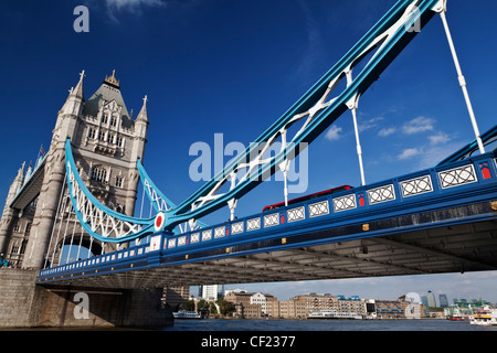 Un rosso London bus attraversando il fiume Tamigi oltre il Tower Bridge, uno di Londra più famosi e iconici punti di riferimento. Foto Stock