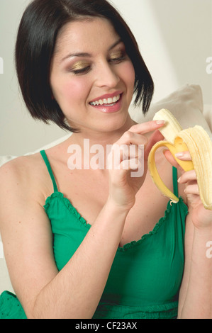 Femmina con lunghezza mento dritto brunette capelli mangiando una banana, sorridere mostrando i denti Foto Stock