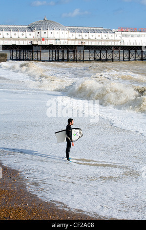 Un lone surfer sta guardando al mare sulla spiaggia di Brighton. Foto Stock