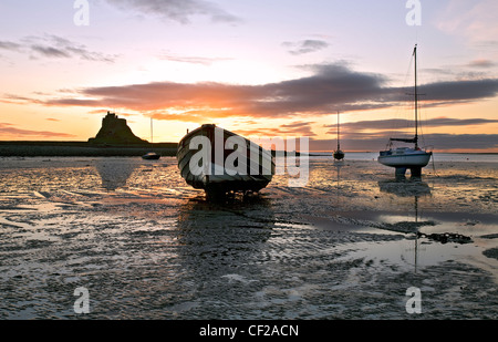 Alba sulle barche ormeggiate a bassa marea con una vista al castello di Lindisfarne. Foto Stock