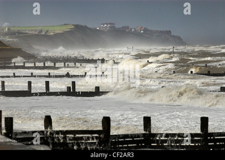 Grandi onde che si infrangono su pennelli sulla spiaggia vicino al villaggio costiero di Mundesley. Foto Stock