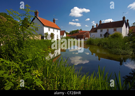 Cottages riflessi nel laghetto presso il Vescovo Burton. Foto Stock