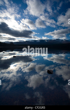 Nuvole drammatico e Monti Cairngorm riflettuto la faccia ancora di Loch Morlich. Foto Stock