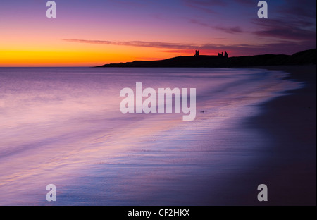 Un display a colori di pre-alba colori relected sulla sabbia bagnata di Embleton Bay, dominato dalle rovine drammatiche di Dunstan Foto Stock