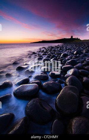 Onde infrangersi contro il mare rocce scolpite che domina la costa di Embleton Bay, dominato dalle rovine drammatiche di Dunsta Foto Stock