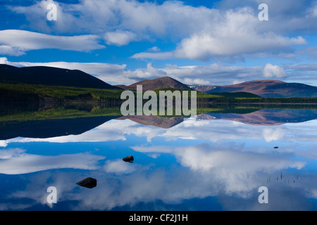 Nuvole, la foresta e la montagna si riflette sulle acque tranquille del Loch Morlich nel Parco Nazionale di Cairngorms. Foto Stock