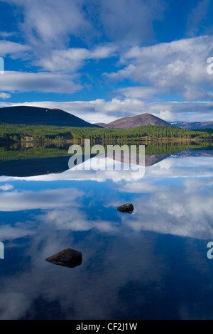 Nuvole, la foresta e la montagna si riflette sulle acque tranquille del Loch Morlich nel Parco Nazionale di Cairngorms. Foto Stock