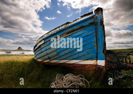 Una vecchia barca da pesca sull Isola Santa con Lindisfarne Castle, costruito dal Re Enrico VIII a guardia della flotta ancoraggio in porto Foto Stock