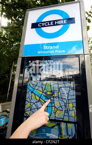 Close-up di una mano alle persone sottolineando la loro posizione su una mappa in corrispondenza di un terminale di un Barclays Cycle Hire docking station. Foto Stock