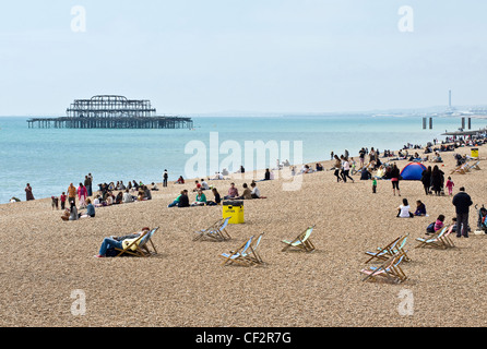 Persone rilassante sulla spiaggia di Brighton con i resti del molo Ovest in background. Foto Stock
