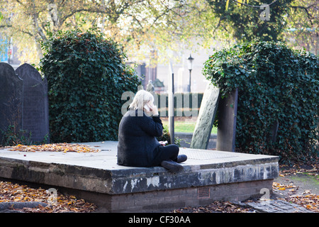 Donna colloqui sul suo telefono cellulare mentre seduto in un cimitero. Foto Stock