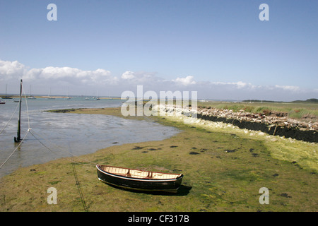 Un piccolo di legno nero barca a remi legata a un grande polo di legno, seduti su una spiaggia sabbiosa di alghe marine patch coperto di terra a bassa marea, Foto Stock