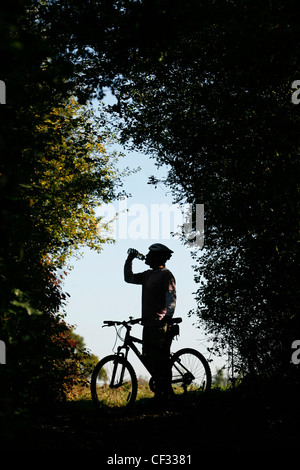 Silhouette di un mountain biker di bere dalla sua acqua in bottiglia. Foto Stock