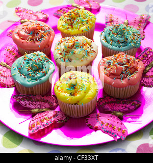 Vivacemente colorato tortine con spruzza sul rosa luminoso piastra con farfalle decorative, macchiato la tovaglia Foto Stock