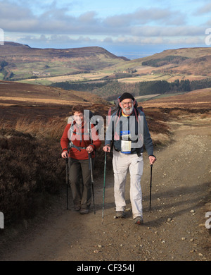 Coppia senior escursionismo con pali trekking o bastoni lungo la strada di Cleveland North Yorkshire Moors England Regno Unito Foto Stock