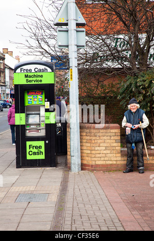 Uomo vecchio, tramp si fermò accanto a un free cash macchina su Lincoln City High Street Foto Stock