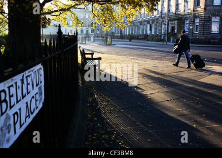 Un uomo tirando una valigia nella luce del mattino su Bellevue Place di Edimburgo. Foto Stock