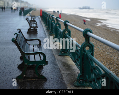 Una linea di panche sul lungomare di Brighton in un giorno di pioggia con il molo di distanza. Foto Stock