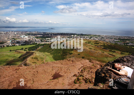 Un uomo a prendere il sole sulla Arthur' Seat si affaccia Edimburgo e il Firth of Forth. Foto Stock