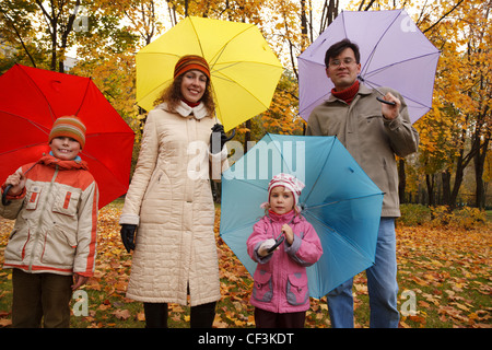Famiglia da 4 persone in autunno park con multi-ombrelloni colorati. Foto Stock