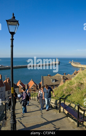 Persone salire a piedi a Whitby famoso '199 passi con il porto e il molo fari in background. Foto Stock