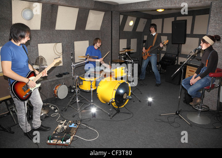 Una rock band. Il cantante ragazza, due musicisti con electro chitarre e un batterista che lavorano in studio. lampeggia in centro Foto Stock