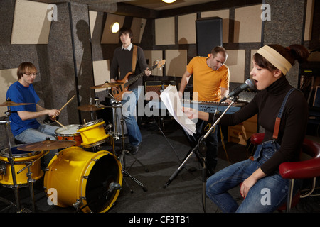 Una rock band sta lavorando in studio. la cantante ragazza è cantare con il testo della canzone nella sua mano Foto Stock